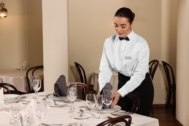 Photo of Woman setting table in restaurant. Professional butler courses