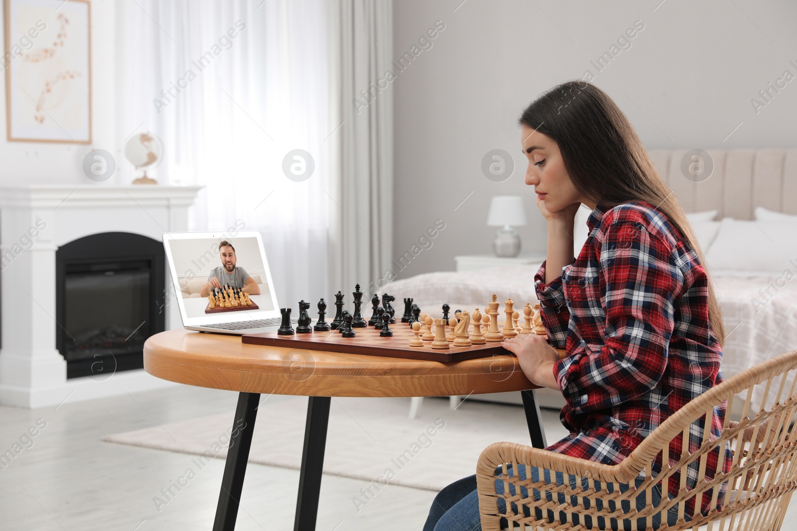 Image of Young woman playing chess with partner via online video chat at home