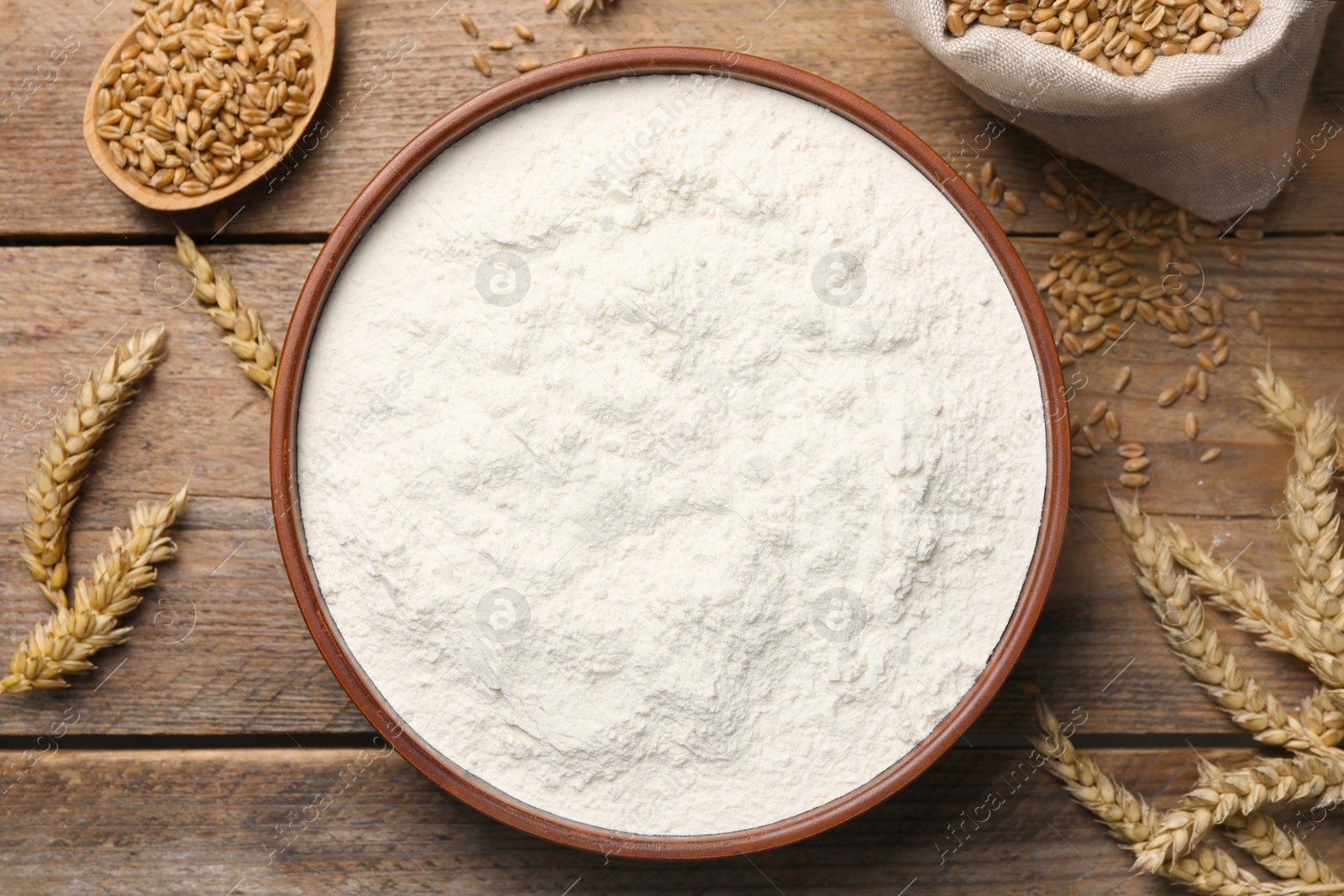 Photo of Wheat flour in bowl, spikes and grains on wooden table, flat lay