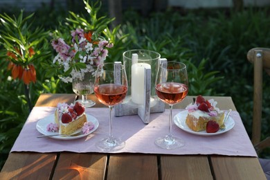 Vase with spring flowers, wine and cake on table served for romantic date in garden