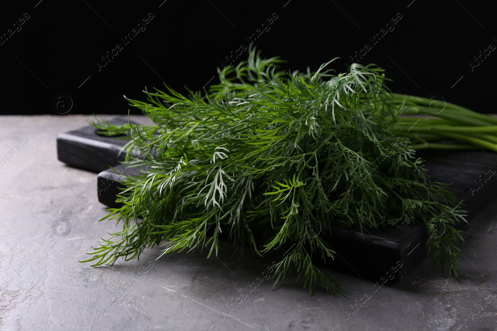 Photo of Board with sprigs of fresh dill on grey textured table against black background, closeup