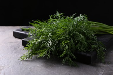 Board with sprigs of fresh dill on grey textured table against black background, closeup