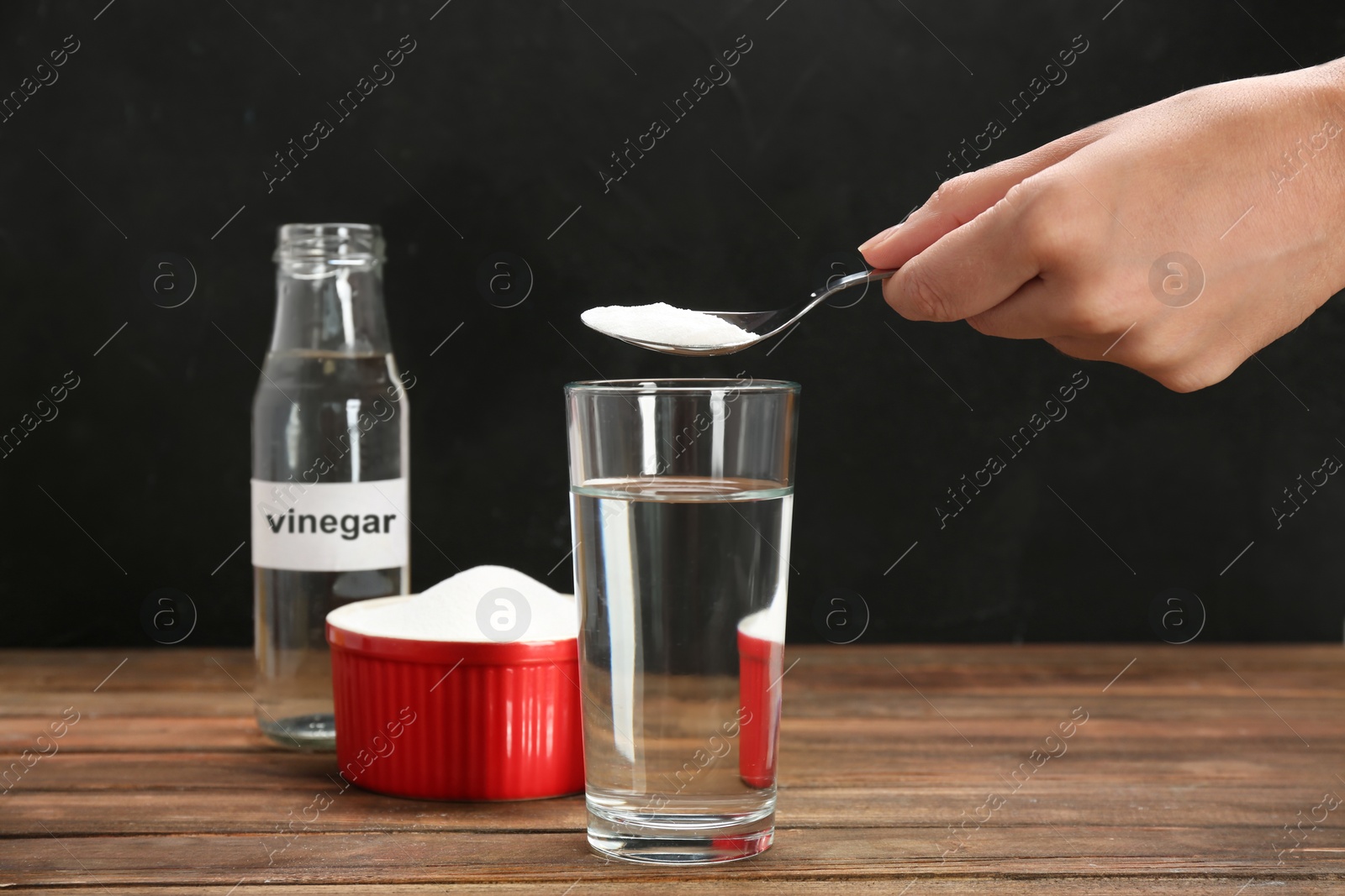 Photo of Woman putting baking soda into glass on wooden table