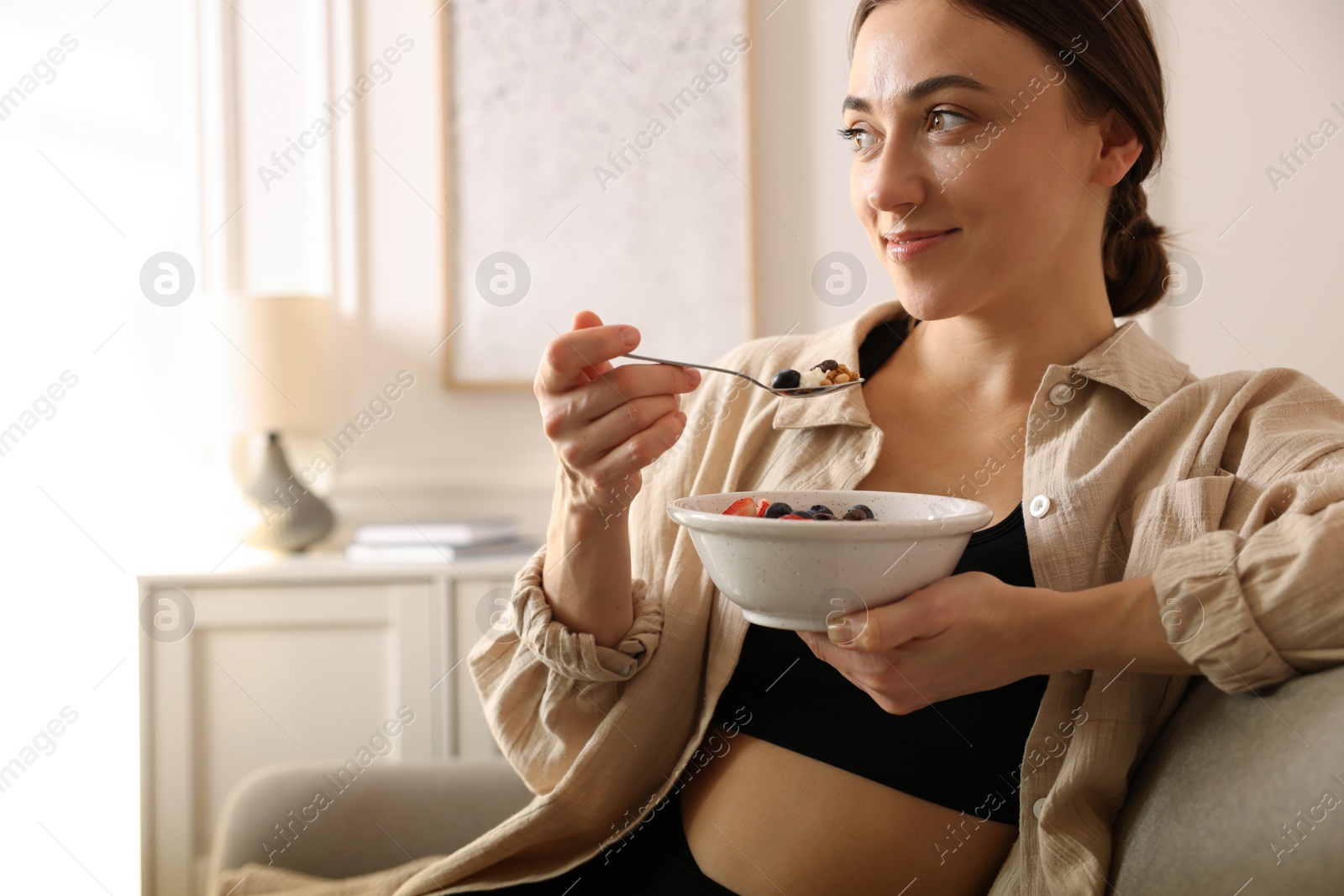 Photo of Woman eating tasty granola with fresh berries and yogurt at home