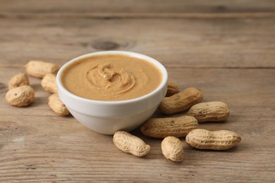 Photo of Delicious nut butter in bowl and peanuts on wooden table, closeup