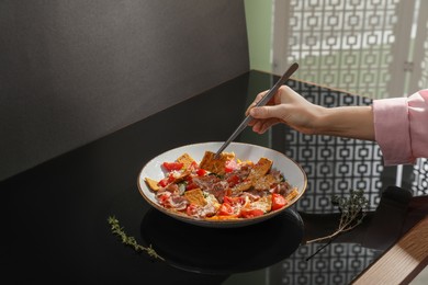 Photo of Food stylist decorating salad with crispy bread at black table in studio, closeup