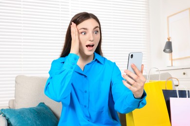 Special Promotion. Emotional woman with smartphone on sofa indoors