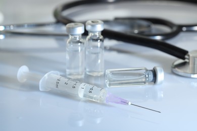 Glass vials, syringe and stethoscope on white table, closeup