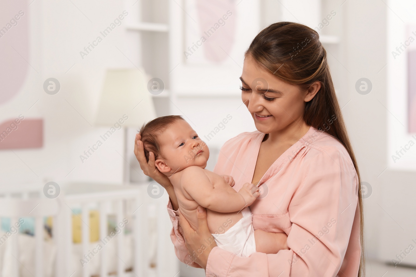 Photo of Mother holding her cute newborn baby in child's room, space for text