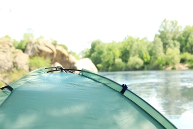 Modern camping tent on riverbank. Space for text