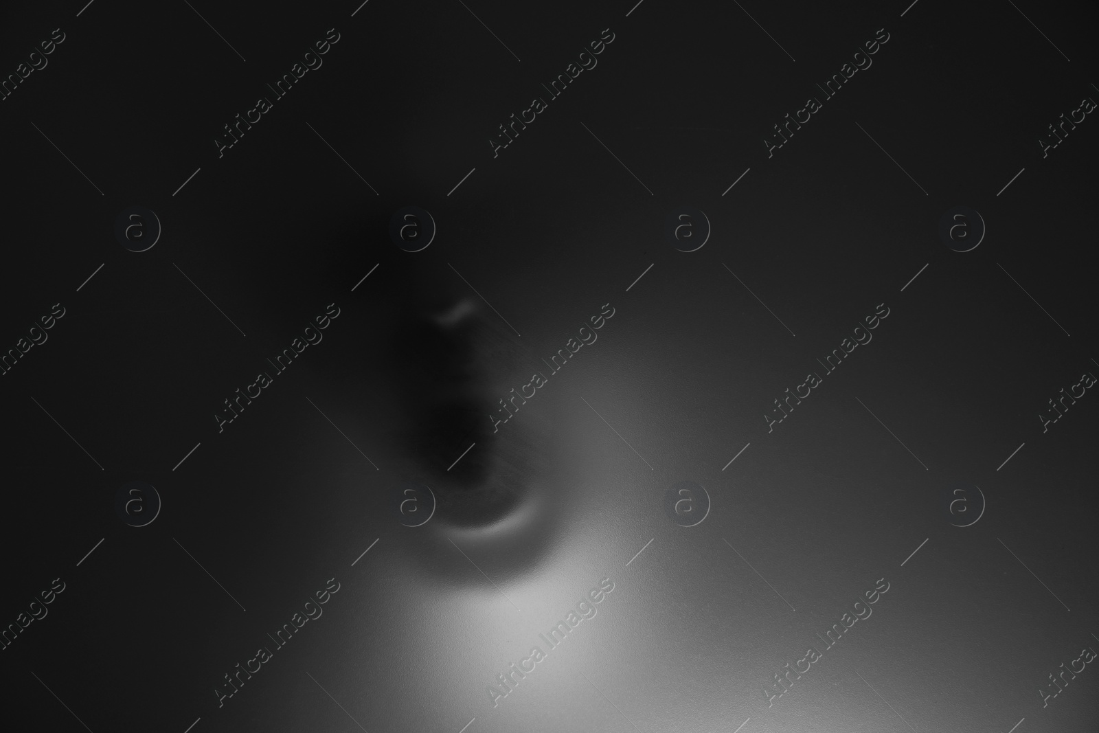 Photo of Silhouette of creepy ghost behind glass against grey background