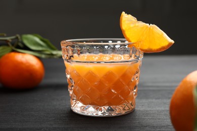 Photo of Tasty tangerine liqueur in glass and fresh fruits on black wooden table, closeup
