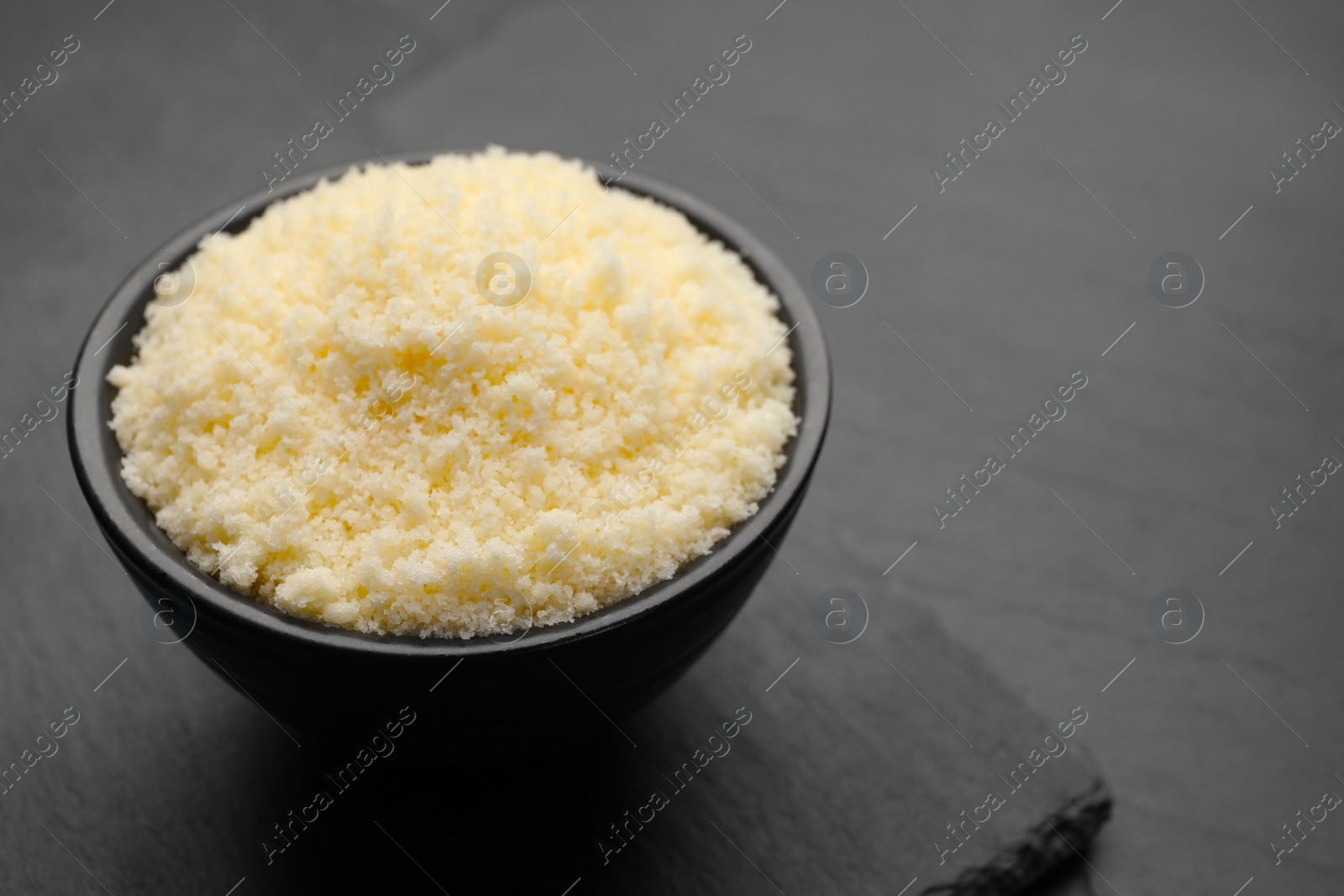 Photo of Bowl with grated parmesan cheese on black table, closeup. Space for text