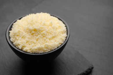 Bowl with grated parmesan cheese on black table, closeup. Space for text