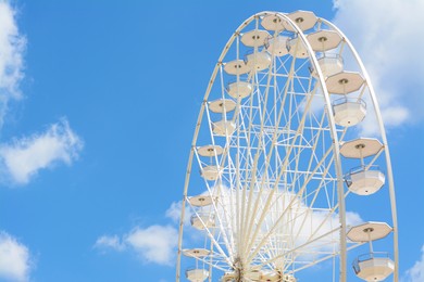 Photo of Large white observation wheel against blue cloudy sky, space for text