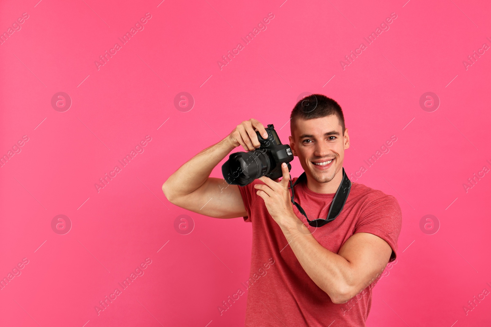 Photo of Young photographer with professional camera on pink background