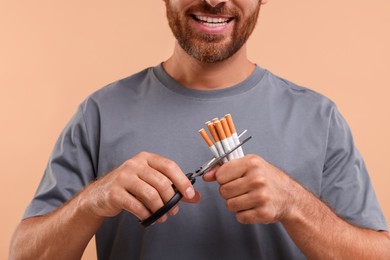 Photo of Stop smoking concept. Man cutting cigarettes on light brown background, closeup
