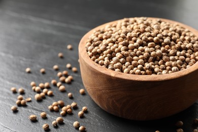 Dried coriander seeds in bowl on dark gray textured table, closeup