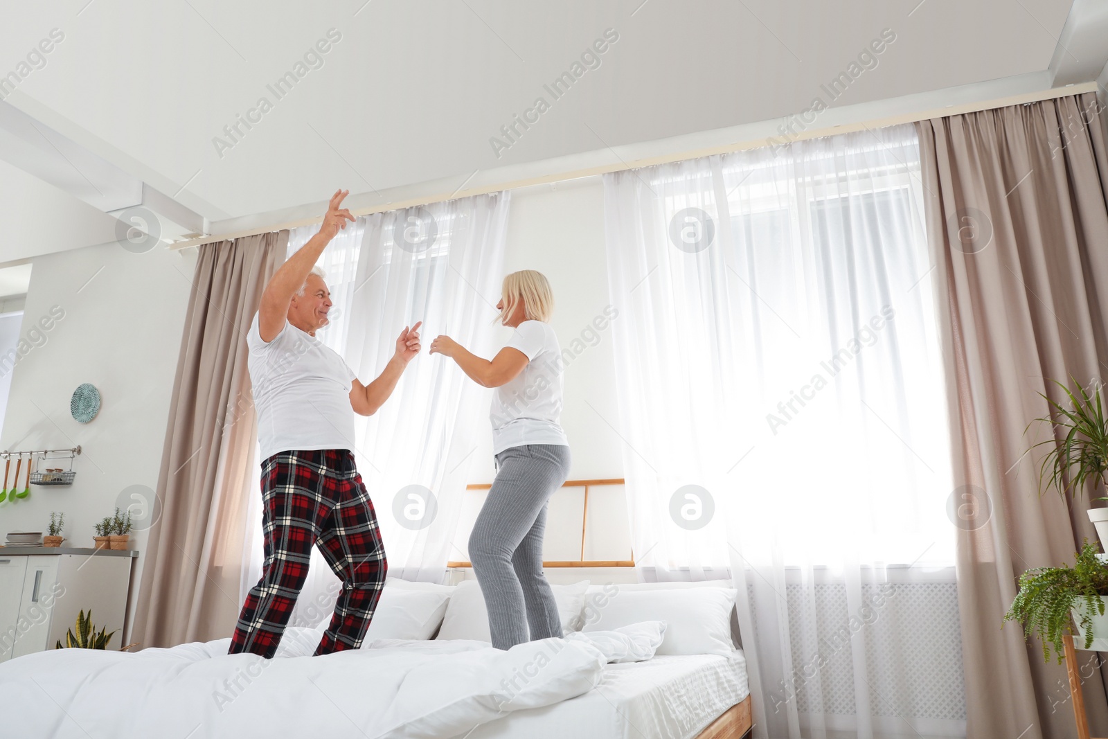 Photo of Happy mature couple dancing together on bed at home
