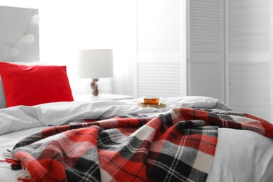 Photo of Comfortable bed with warm checkered plaid in stylish room interior