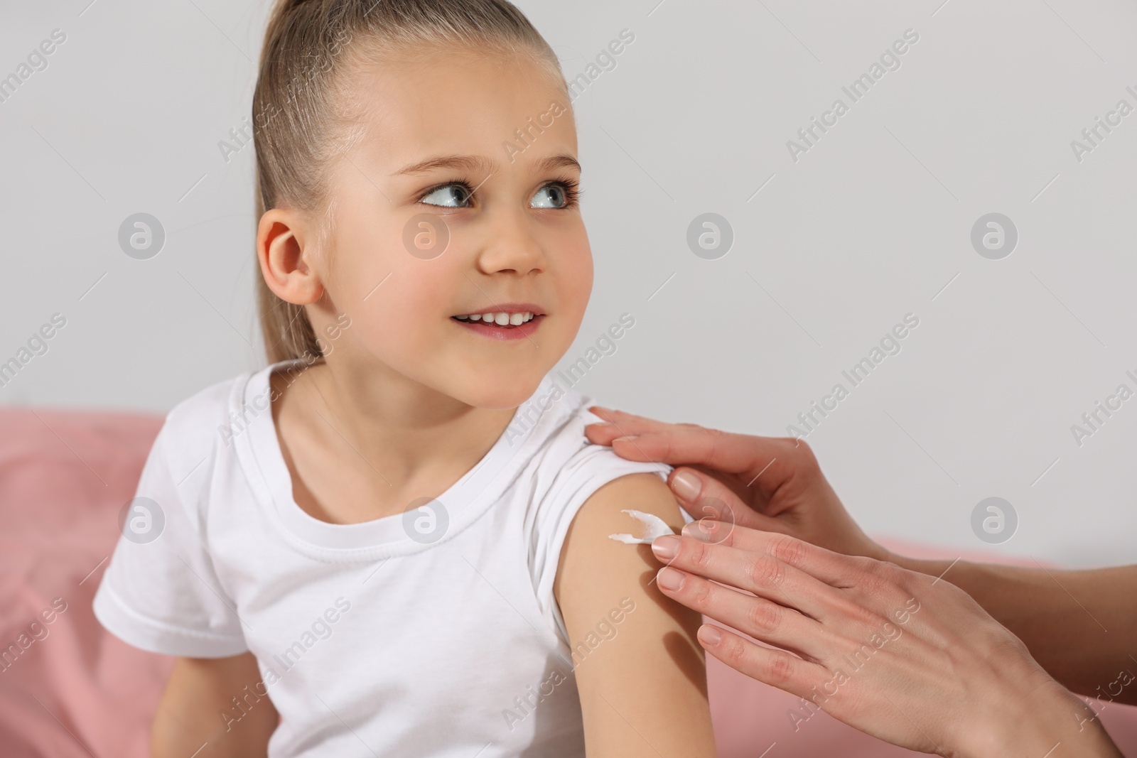 Photo of Mother applying ointment onto her daughter's arm on bed
