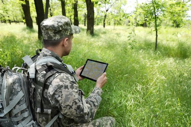 Soldier with backpack using tablet in forest