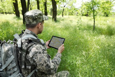 Photo of Soldier with backpack using tablet in forest