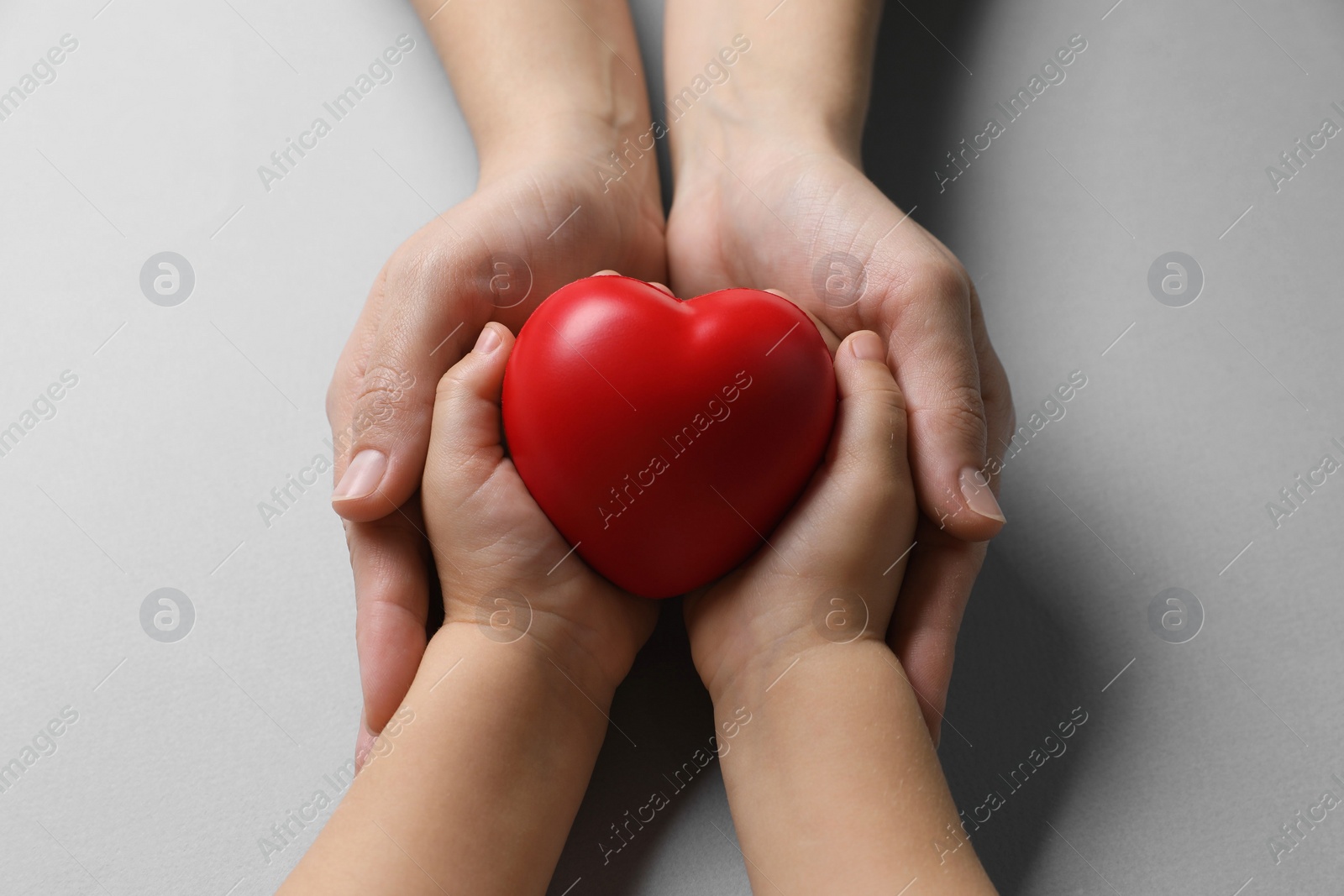 Photo of Mother and her child holding red decorative heart on gray background, top view