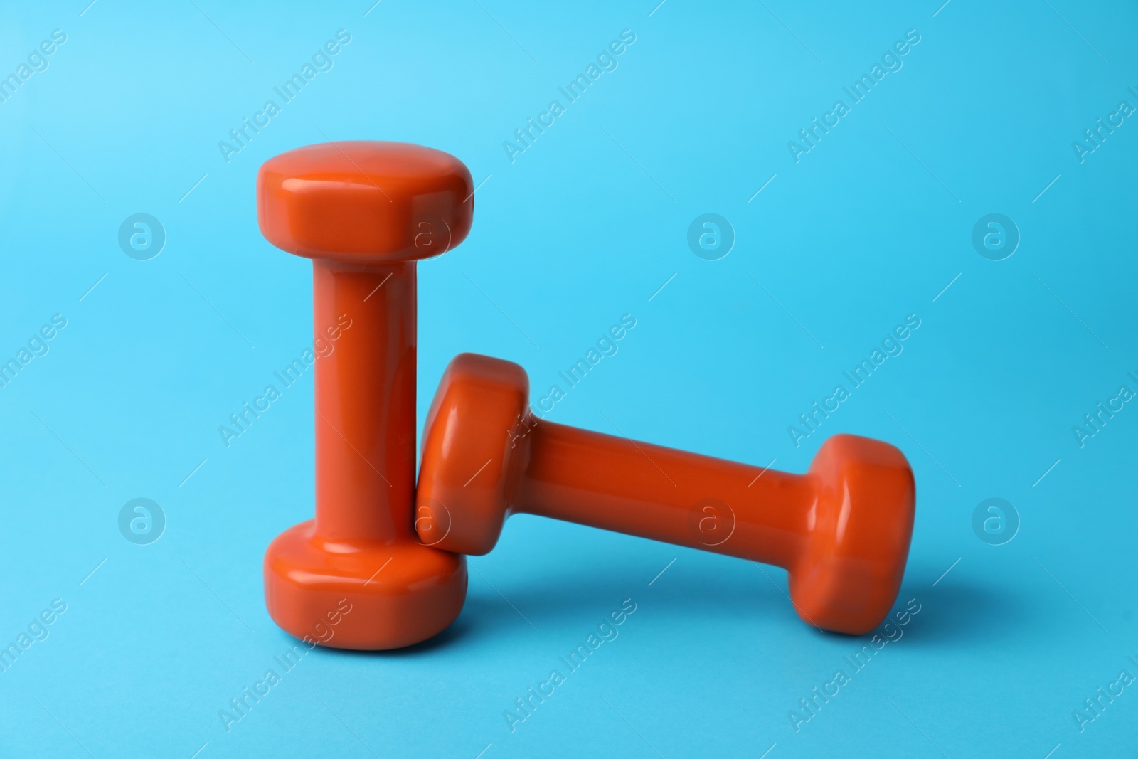 Photo of Stylish orange dumbbells on light blue background