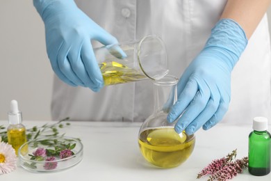 Scientist developing cosmetic oil at white table, closeup