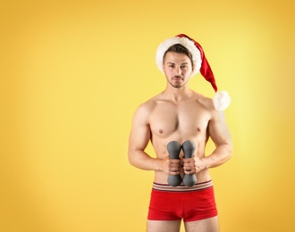 Photo of Shirtless sexy young Santa Claus with dumbbells on color background