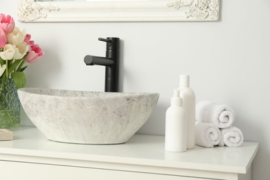 Vase with beautiful pink tulips and toiletries near sink in bathroom