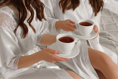 Photo of Bride and her bridesmaid with cups of tea at home, closeup. Wedding day