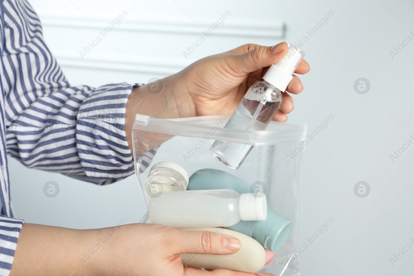 Photo of Woman packing cosmetic travel kit indoors, closeup