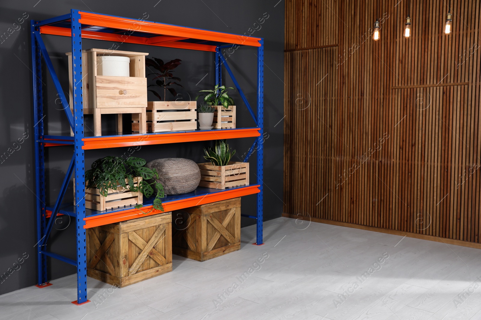 Photo of Metal shelving unit with wooden crates and different household stuff near black wall indoors. Space for text