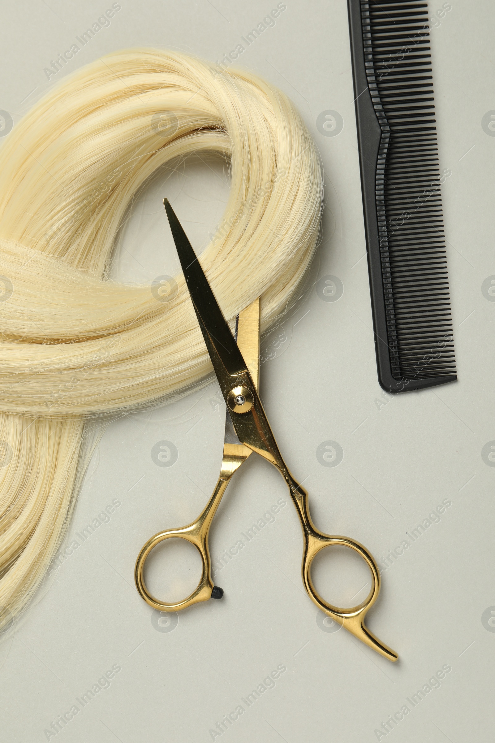 Photo of Professional hairdresser scissors and comb with blonde hair strand on light grey background, flat lay