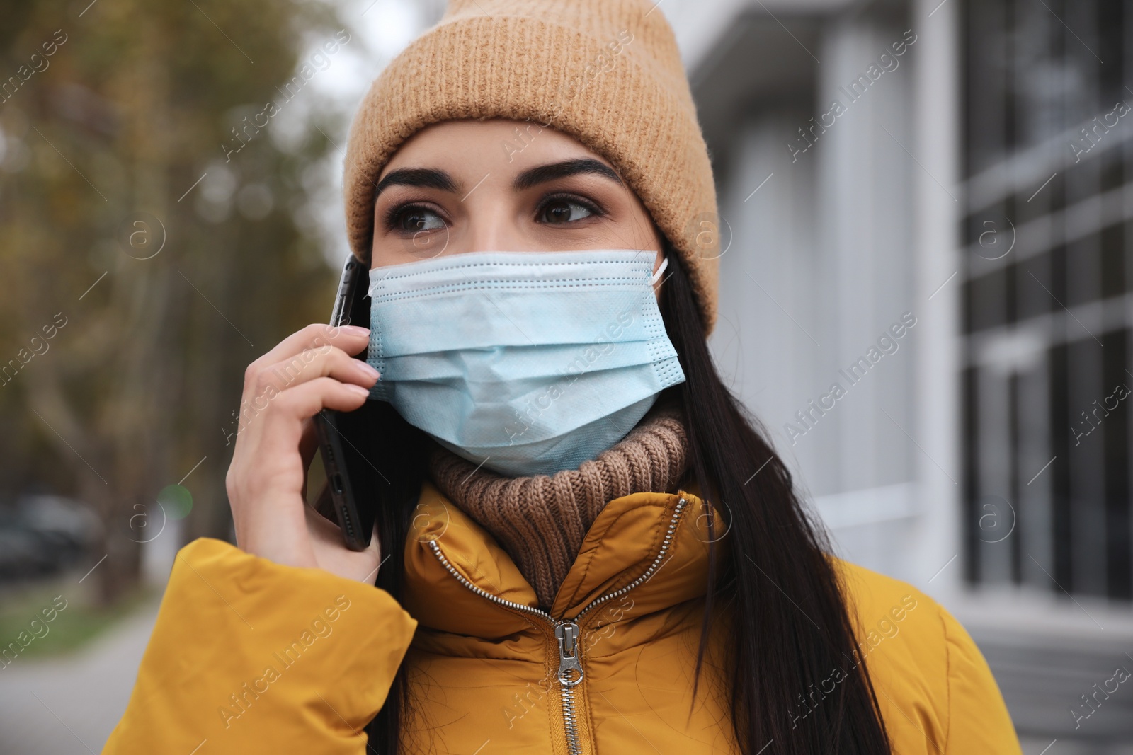 Photo of Young woman in medical face mask talking on phone while walking outdoors. Personal protection during COVID-19 pandemic