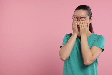 Resentful woman covering face with hands on pink background. Space for text