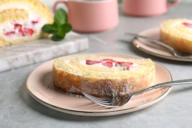 Photo of Slice of delicious sponge cake roll with strawberries and cream served on light grey table, closeup