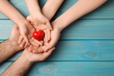 Photo of Parents and kid holding red heart in hands at light blue wooden table, top view. Space for text