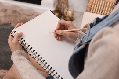 Photo of Young woman drawing in sketchbook at home, closeup