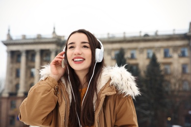 Beautiful young woman listening to music with headphones outdoors. Space for text