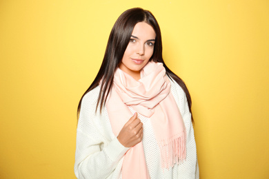 Pretty young woman wearing warm sweater and scarf on yellow background