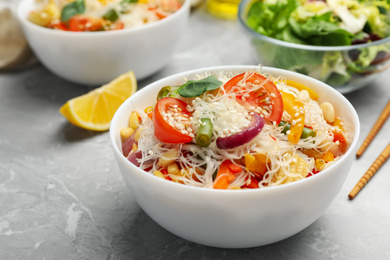 Photo of Tasty cooked rice noodles with vegetables on grey marble table