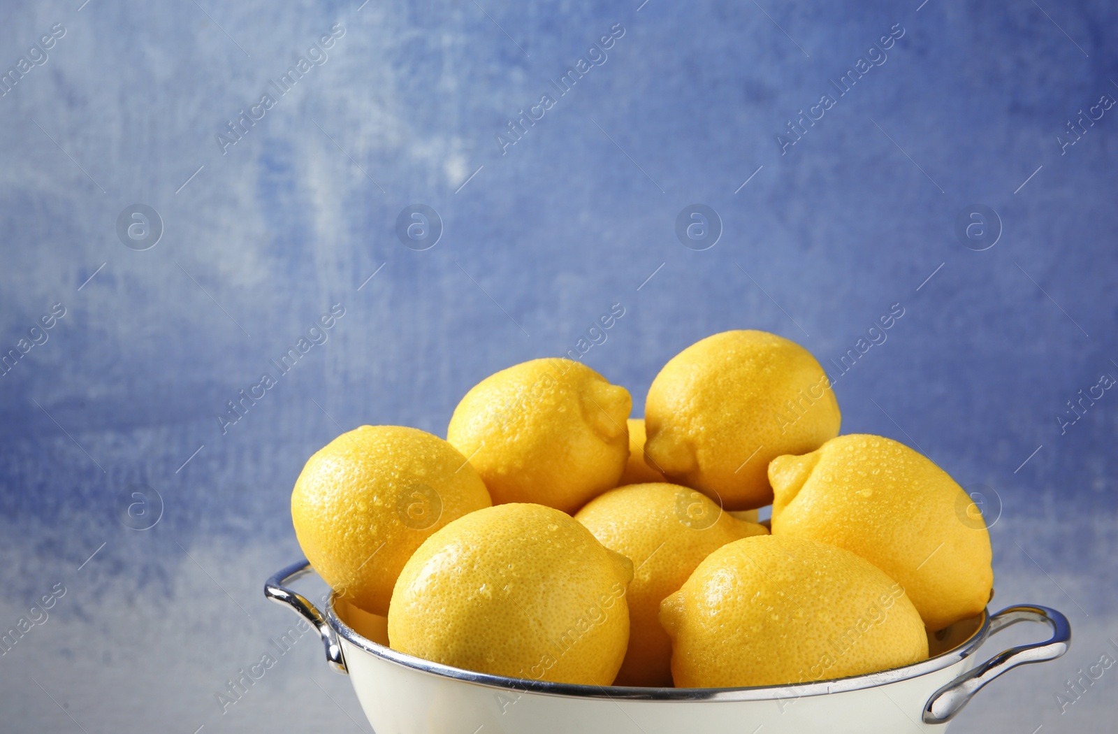 Photo of Colander with ripe lemons against color background