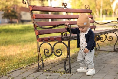 Little baby learning to walk near bench in park