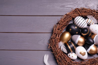 Photo of Festively decorated Easter eggs, vine wreath and feathers on grey wooden table, top view. Space for text