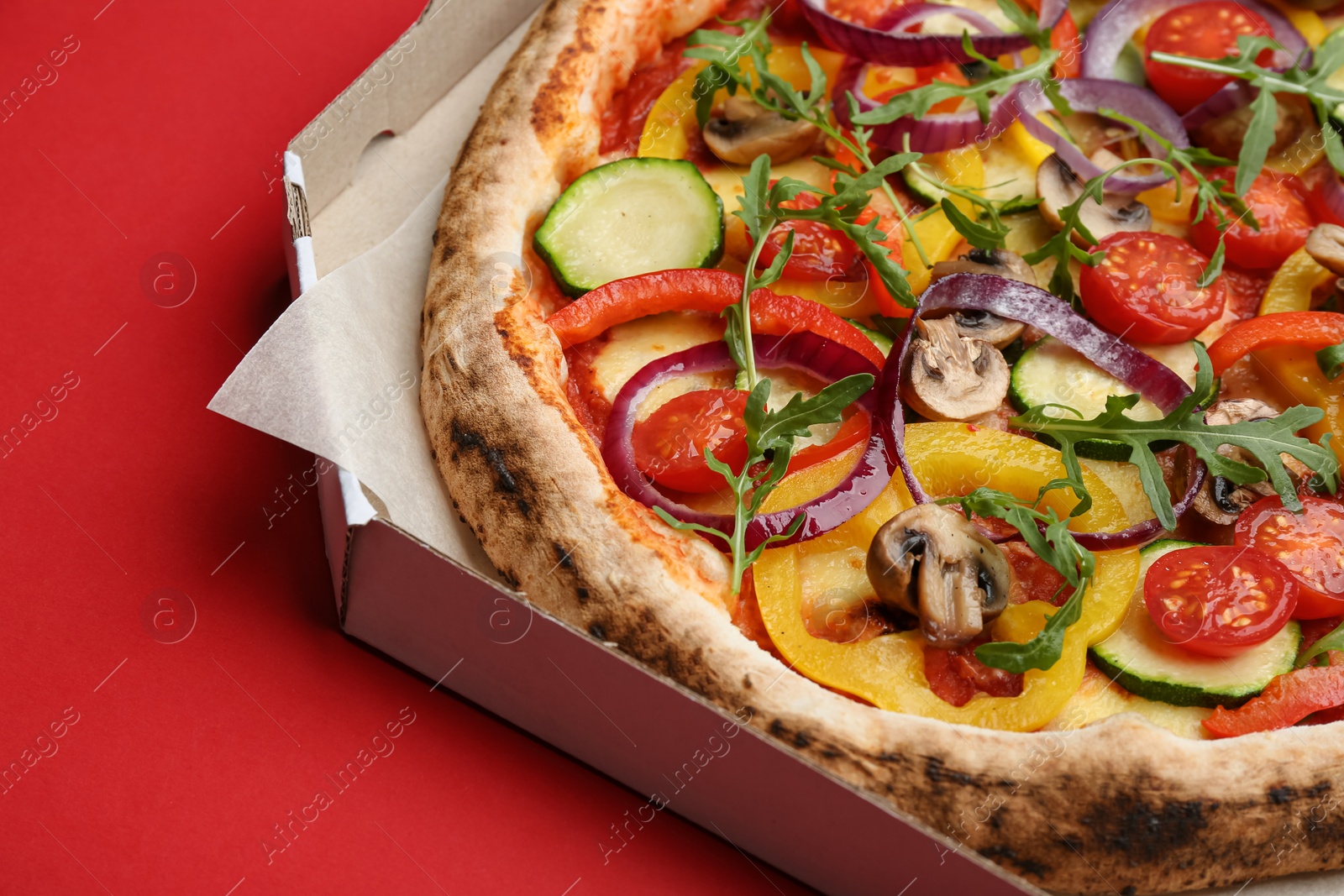 Photo of Delicious vegetable pizza in cardboard box on red background, closeup view