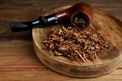 Photo of Board with smoking pipe and dry tobacco on wooden table, closeup