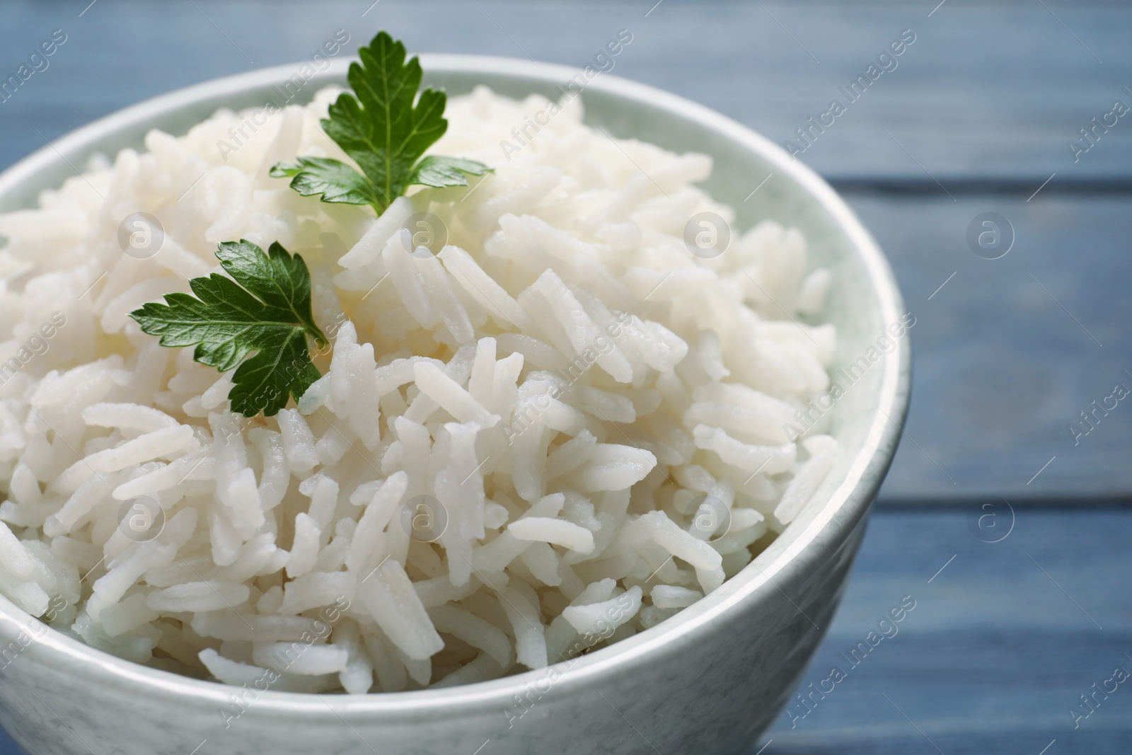 Photo of Bowl of tasty cooked rice with parsley on table, closeup